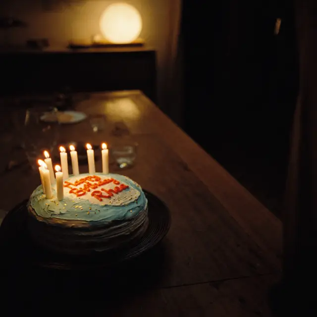 a homemade birthday cake with lit candles on a kitchen table